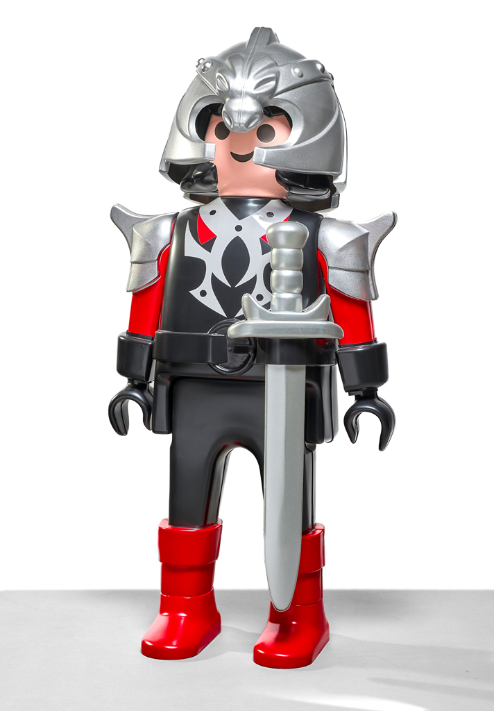 Grande figura giocattolo Playmobil raffigurante un cavaliere. Indossa un’armatura nera e rossa con dettagli argentati, un elmo decorato e stivali rossi lucidi. Tiene una spada argentata davanti a sé